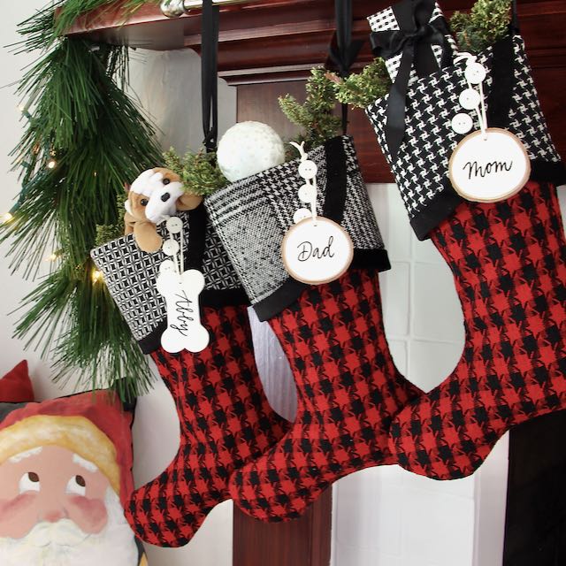 Three similar but unique Christmas stockings hang from a mantel Name tags made from tree slices hang from the top button on each cuff