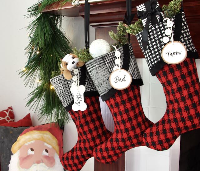 3 coordinating yet unique Christmas stockings are hanging from a mantel. Blue birch slice name tags hang from the top of three buttons on each cuff