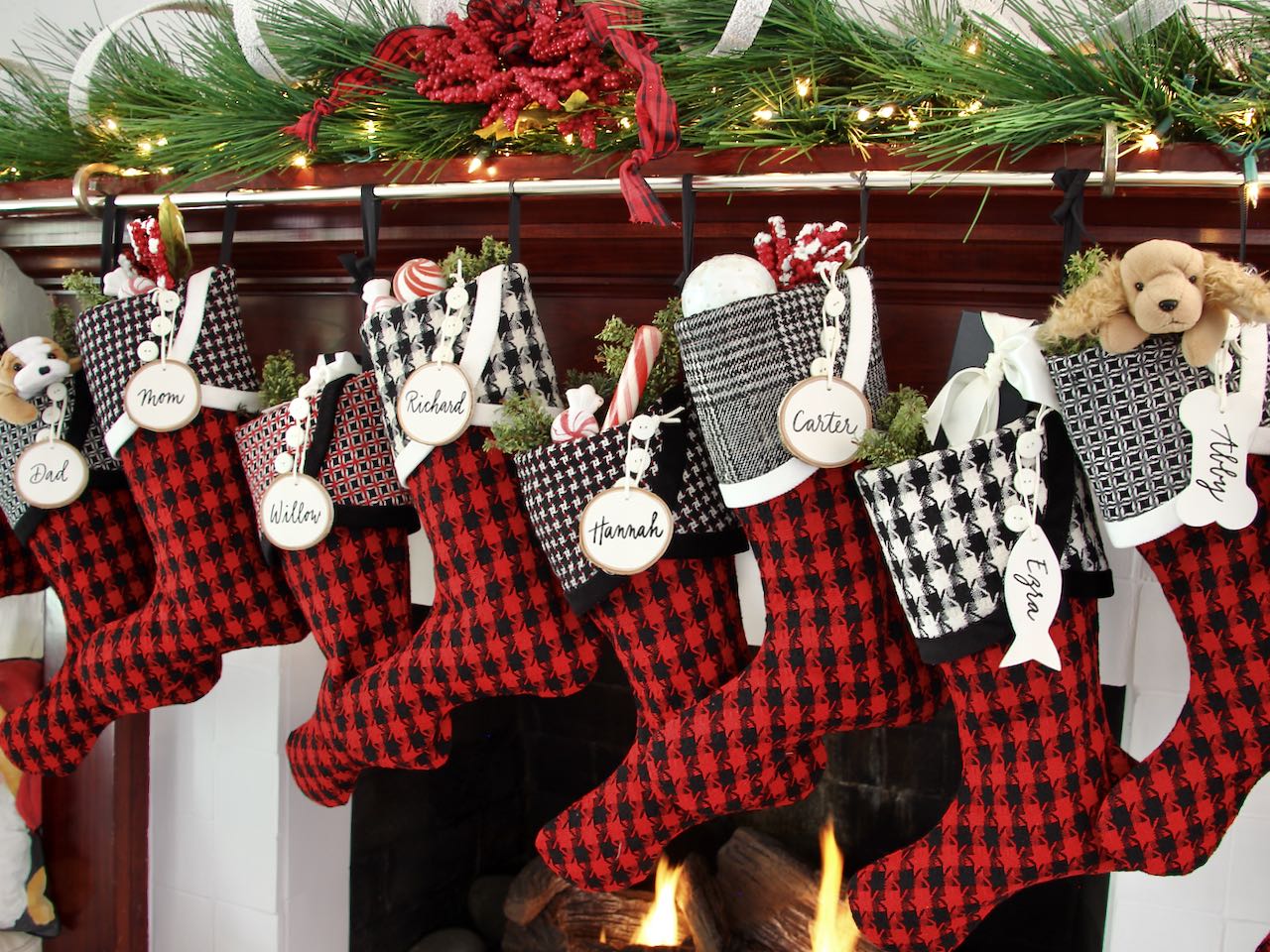 8 coordinating yet unique Christmas stockings are hanging from a mantel above a fire. White tree slice name tags hang from the top of three buttons on each cuff