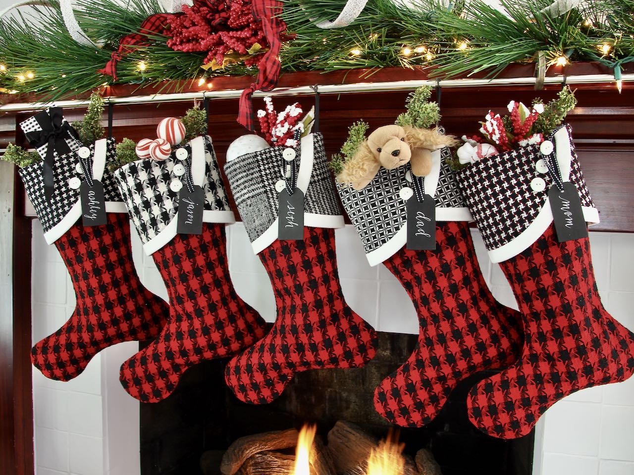 5 coordinating yet unique Christmas stockings are hagning from a mantel above a fire. Black wood name tags hang from the top of three buttons on each cuff