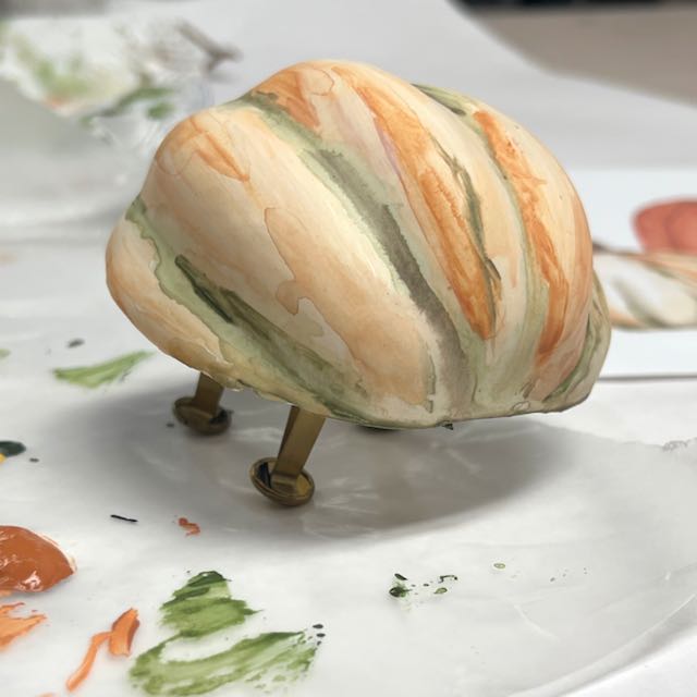 closeup of a freshly painted pumpkin half standing on brad feet while drying