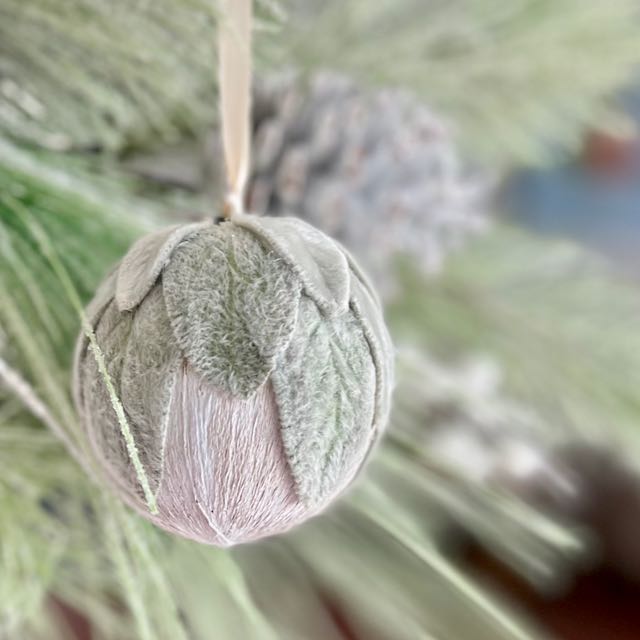 Closeup of an ornament covered in Lamb's Ear leaves is hanging on a fir branch