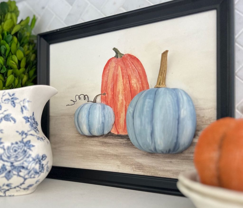 blue and orange 3D pumpkin wall art in a black frame sitting on a kitchen open shelf