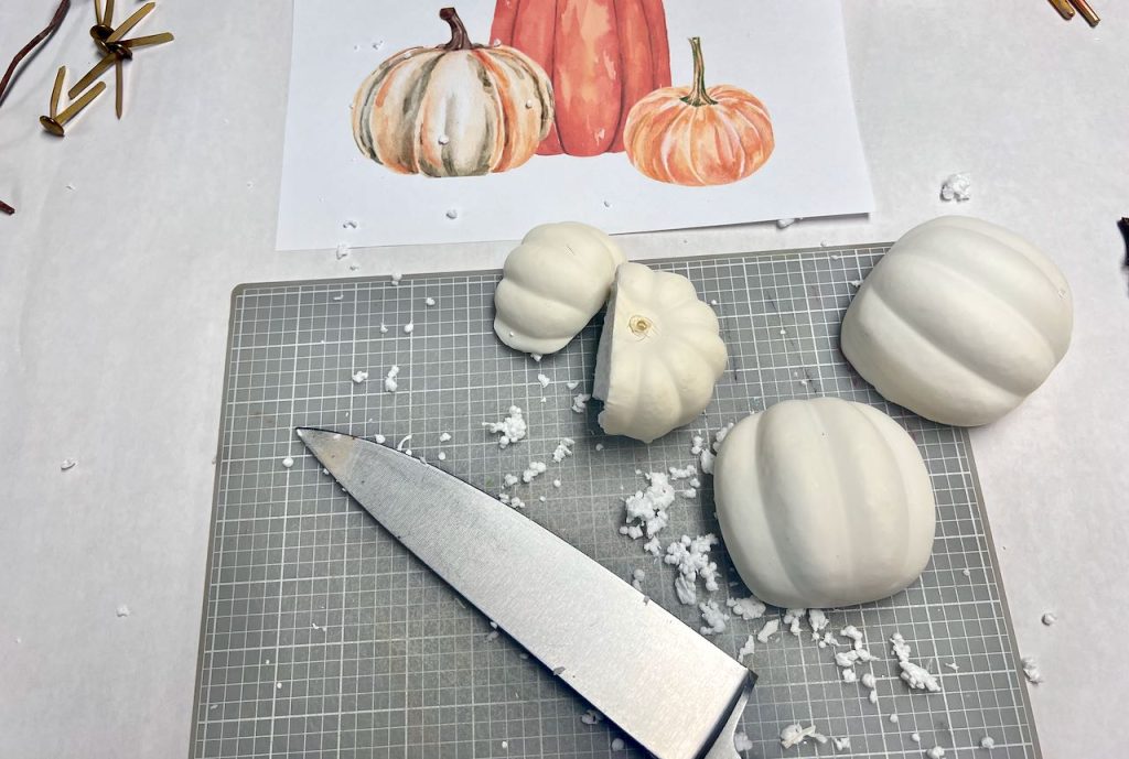 a large knife on a cutting mat is next two to styrofoam pumpkins that have been cut in half