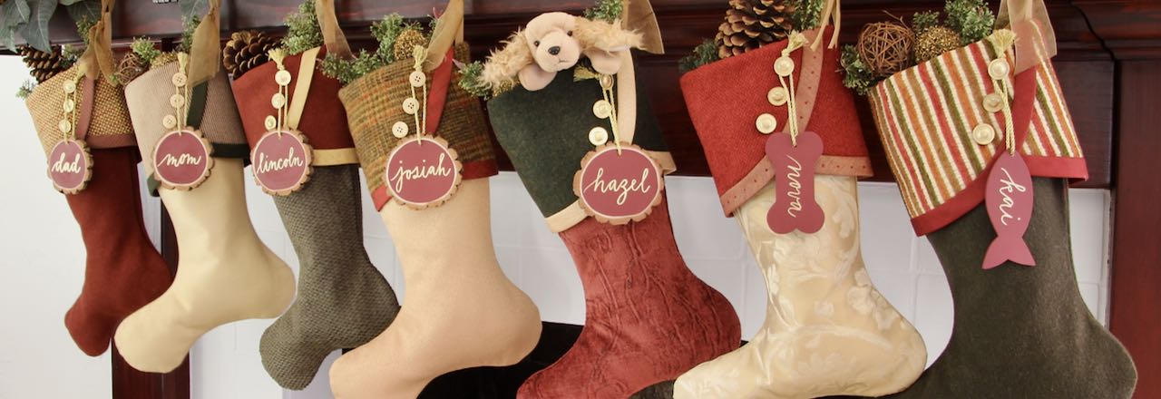 7 coordinating yet unique Christmas stockings are hanging from a mantel above a fire. Tree slice name tags hang from the top of three buttons on each cuff