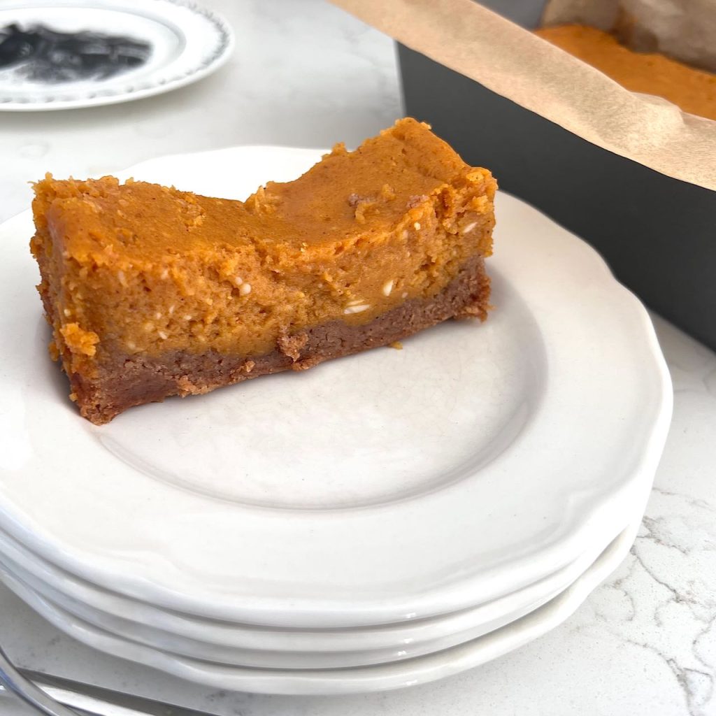 A slice of pumpkin spice ooey gooey butter cake on a plate next to the loaf pan in came out of