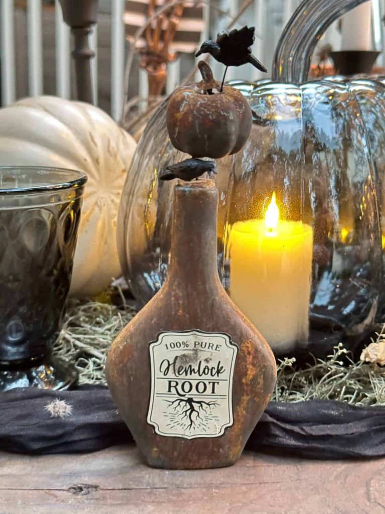 miniature liquor bottle is made over into a rusty bottle with a "Hemlock" label and rusted pumpkin stopper and crow sitting on top