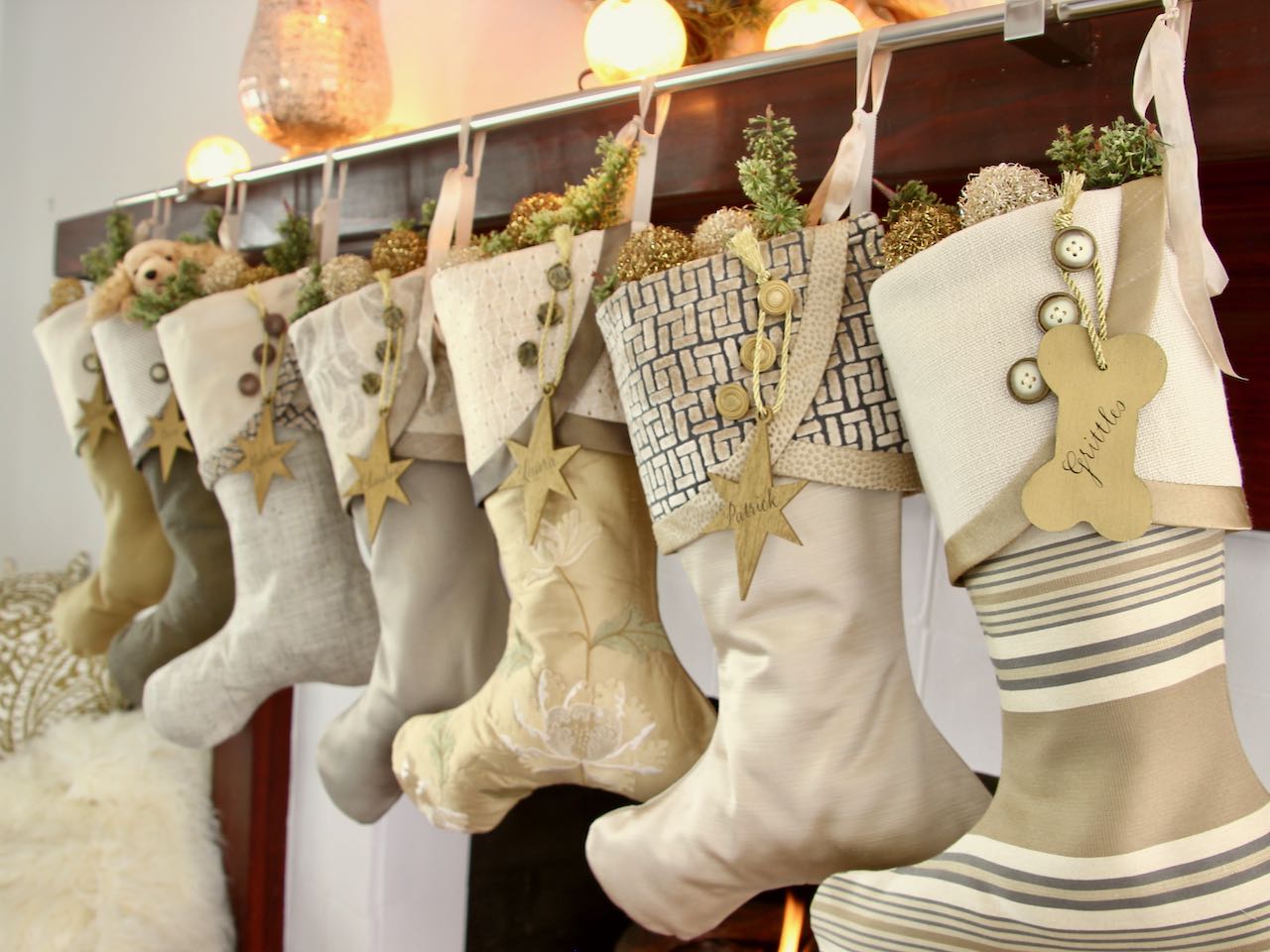7 coordinating yet unique Christmas stockings are hagning from a mantel above a fire. Gold wood star name tags hang from the top of three buttons on each cuff