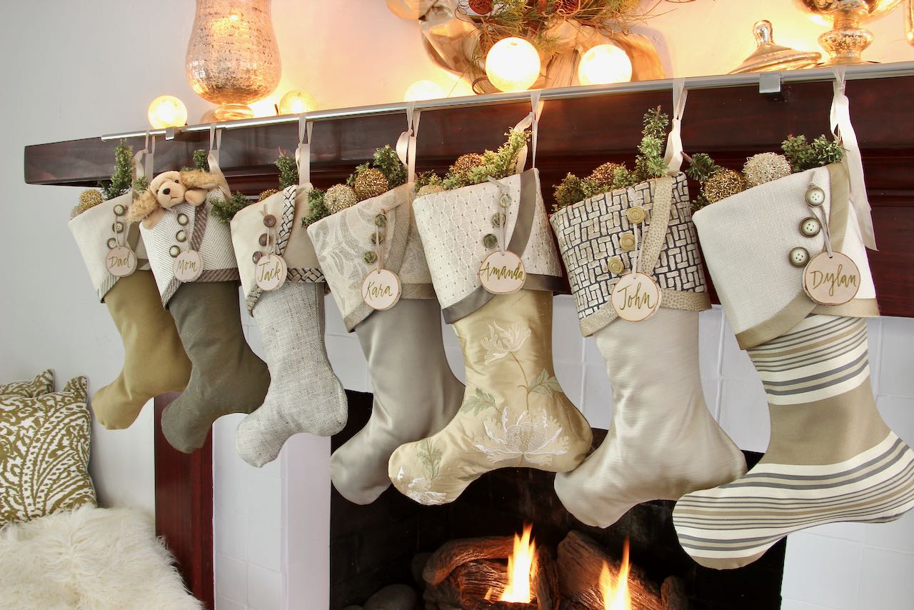 7 coordinating yet unique Christmas stockings are hagning from a mantel above a fire. Birch slice name tags hang from the top of three buttons on each cuff.