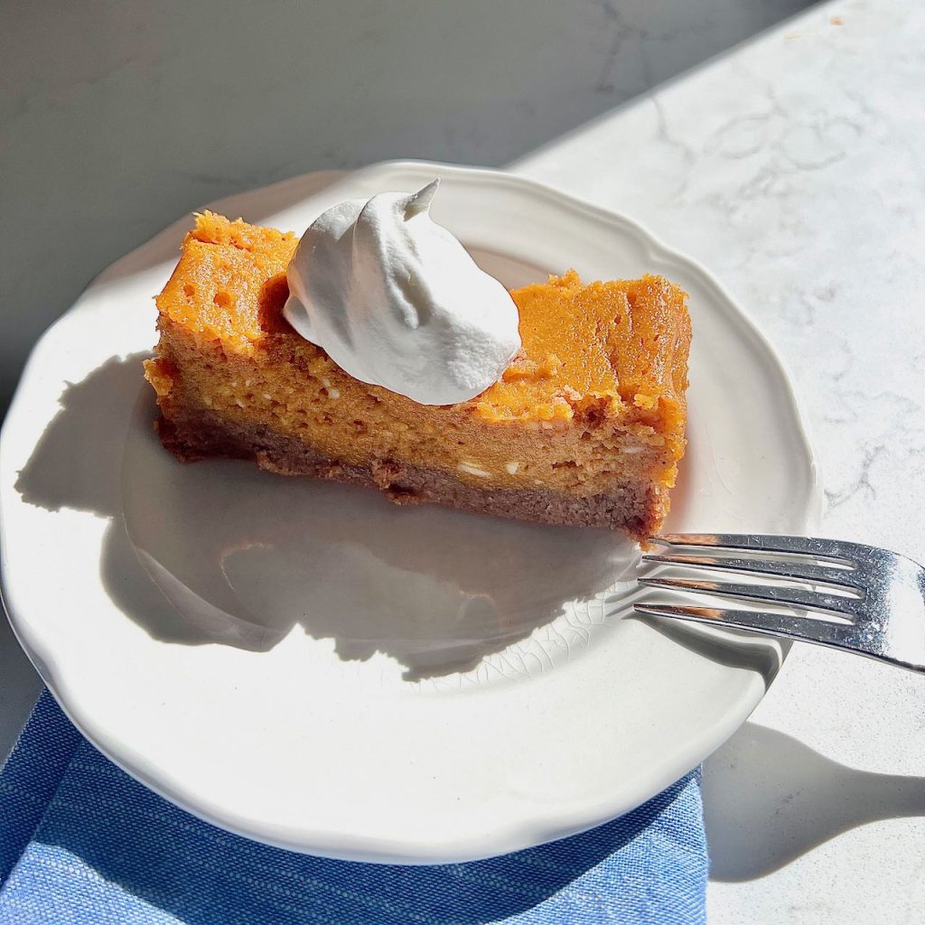 A sloce off pumpkin spice gooey cake with a dollop of whipped cream on top in the bright sunshine