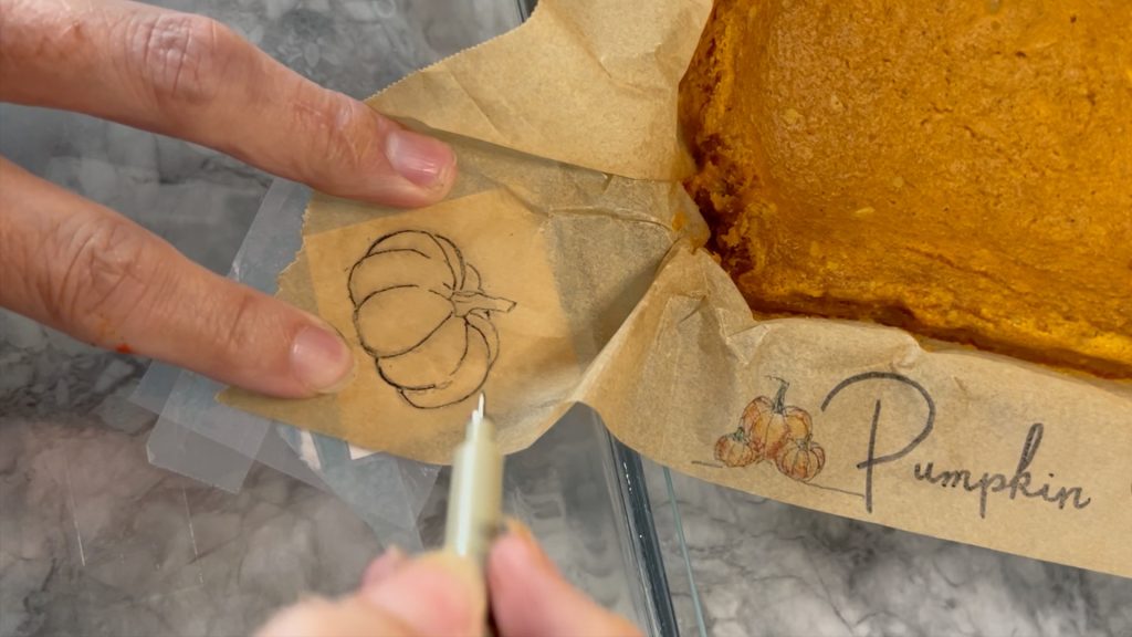 fingers holding parchment paper over the pumpkin pattern while it is being traced