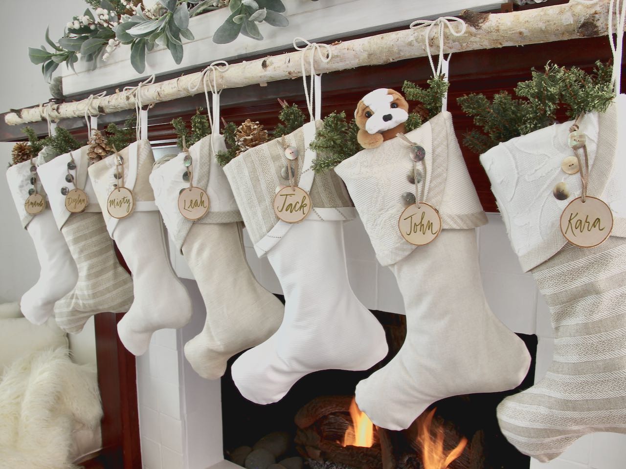 3 coordinating yet unique Christmas stockings are hanging from a mantel above a fire. Birch slice name tags hang from the top of three buttons on each cuff
