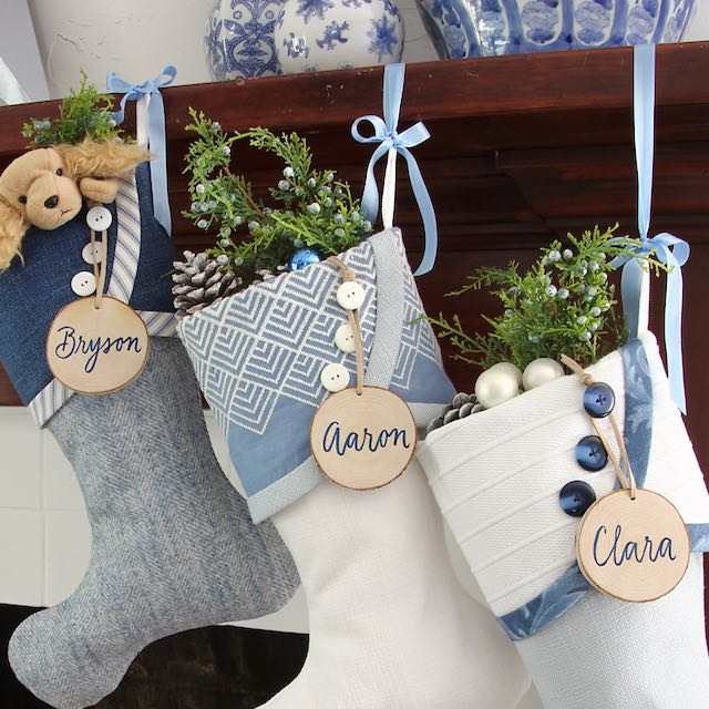 Three similar but unique Christmas stockings hang from a mantel. Name tags made from tree slices hang from the top button on each cuff
