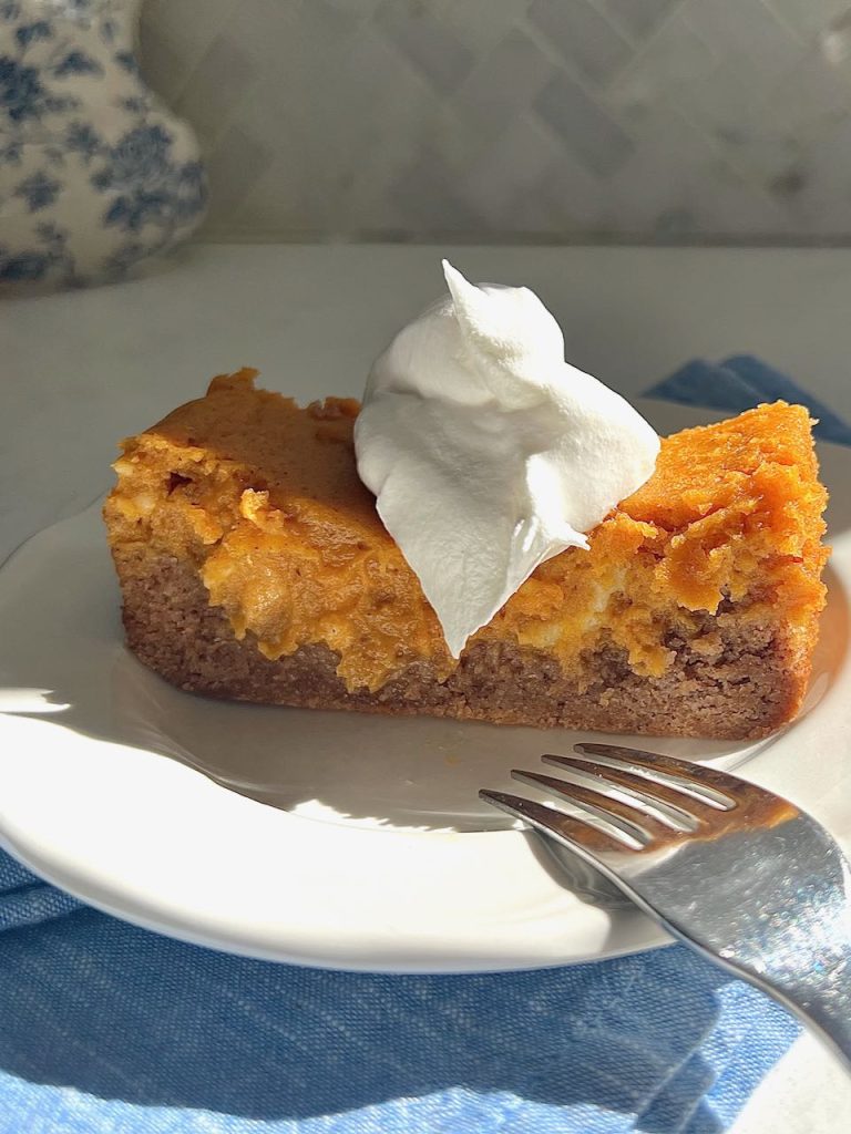 A sloce of pumpkin spice gooey cake with a dollop of whipped cream on top in the bright sunshine