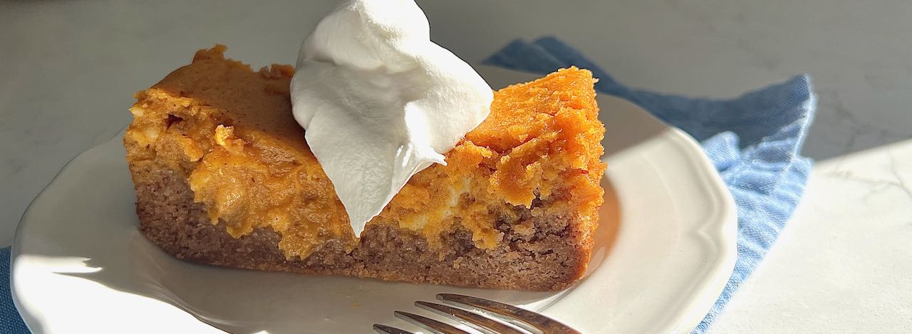 wide closeup of A sloce of pumpkin spice gooey cake with a dollop of whipped cream on top in the bright sunshine