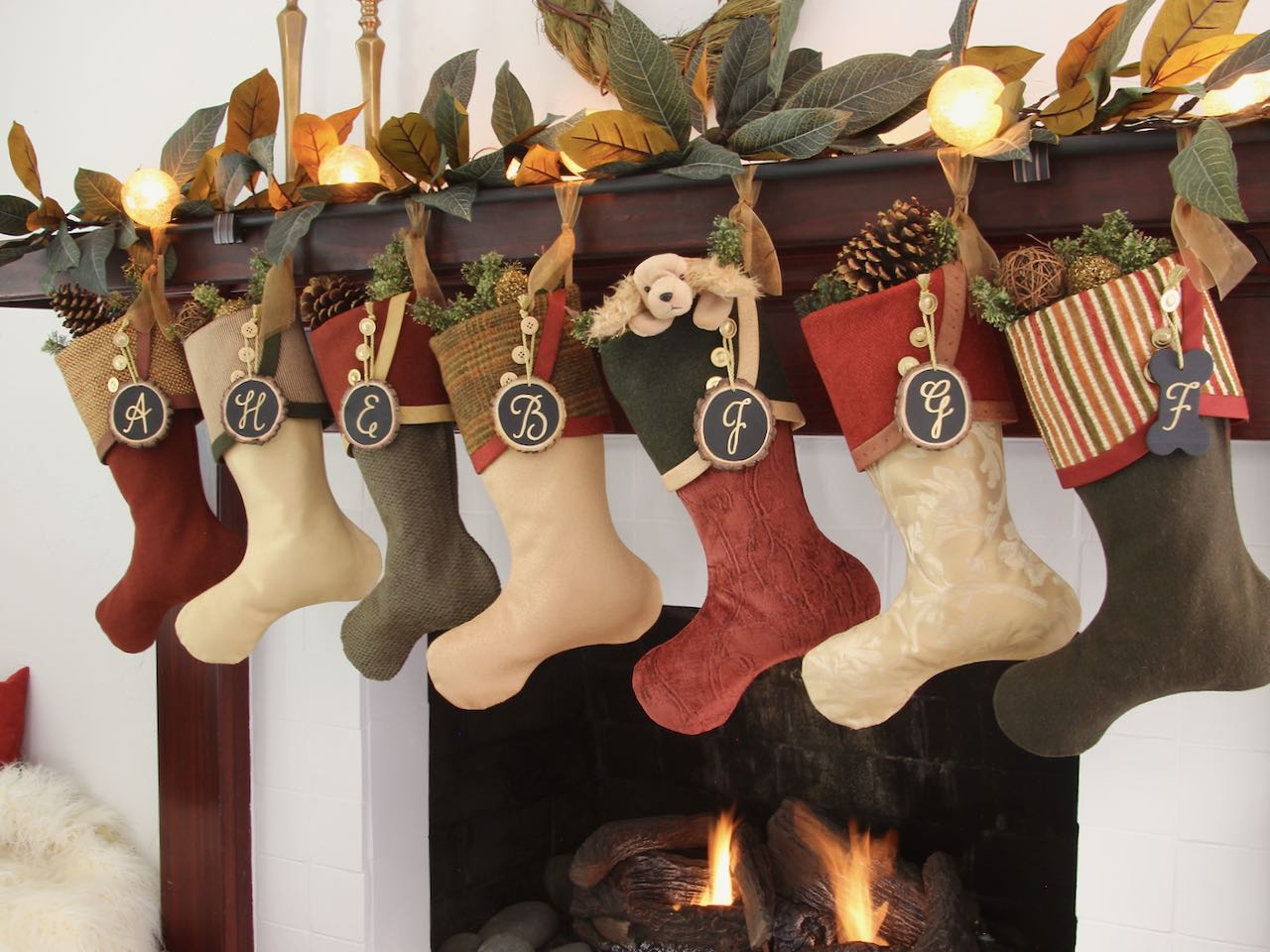 7 coordinating yet unique Christmas stockings are hagning from a mantel above a fire. Tree slice name tags hang from the top of three buttons on each cuff