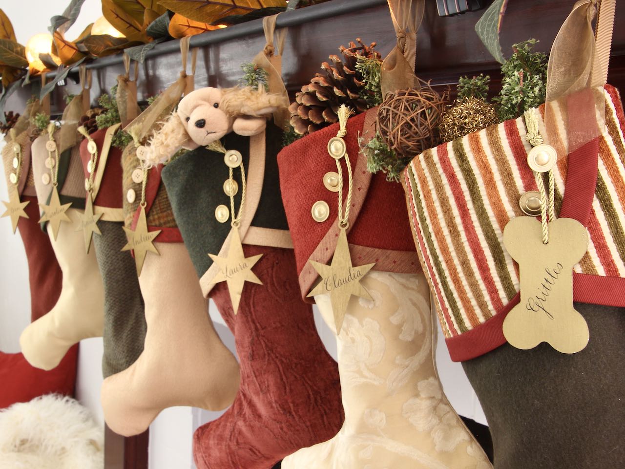 7 coordinating yet unique Christmas stockings are hanging from a mantel. Gold wooden star name tags hang from the top of three buttons on each cuff