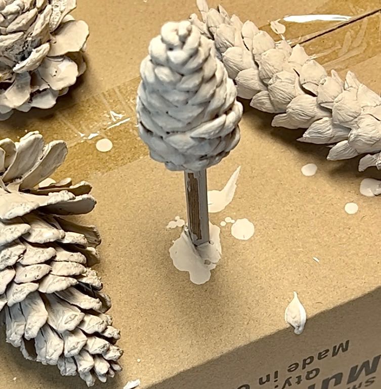 pinecone on a stick is sticking out of a box while its paint dries.