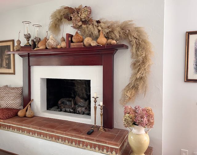 wall-mounted dried arrangement hanging above a mantel with gourds and vintage books. The garland hangs down below thhe mantel on one side