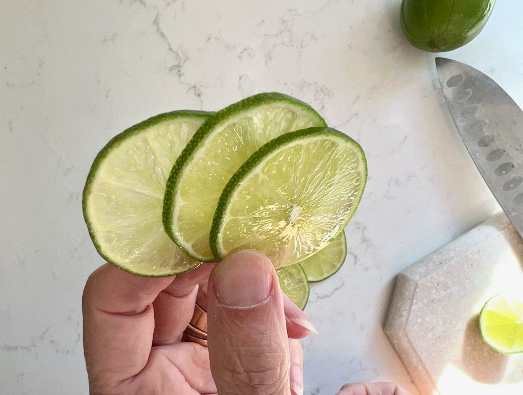 closeup of woman's fingertips holding up three thinly sliced lime slices
