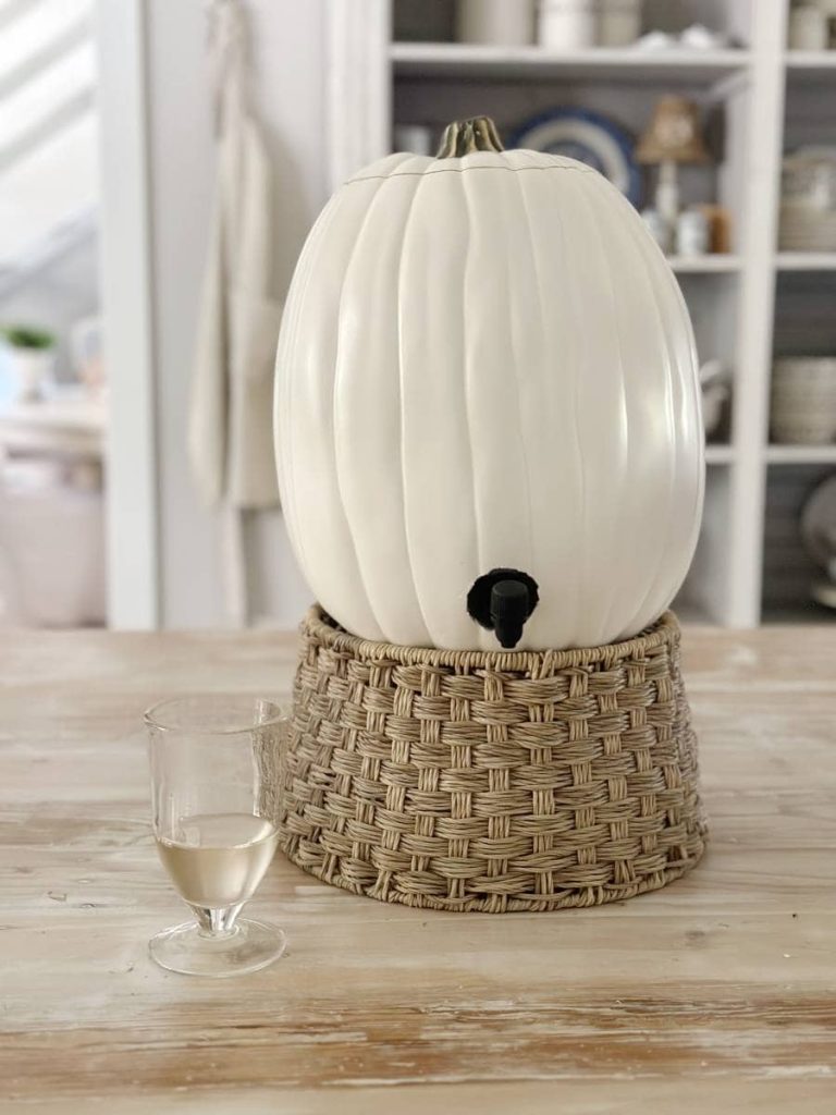 foam pumpkin carved to hold a bag of wine and dispense it from a spigot is sitting on an elevated  basket with a wine glass beside it