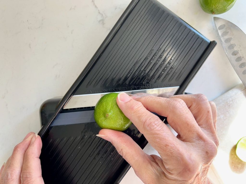 woman's hands showing slicing a fresh lime on a mandolin slicer