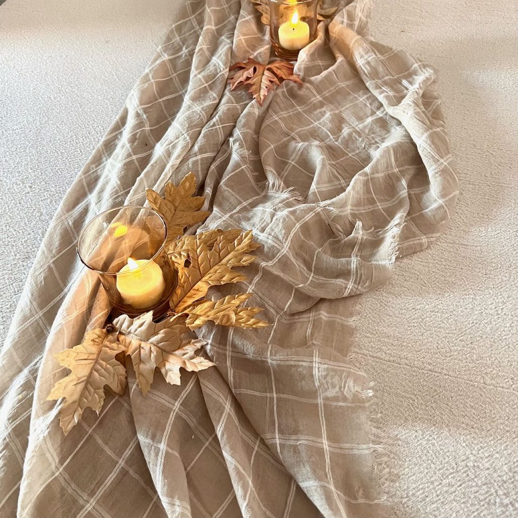 view down length of table with a plaid shawl added as a table runner and votive candles with a few Fall leaves