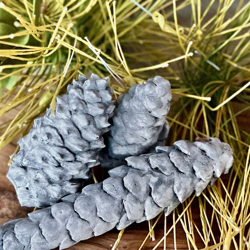 Closeup of three "concrete" pinecone nestled in ssome pine needles on a wood breadboard