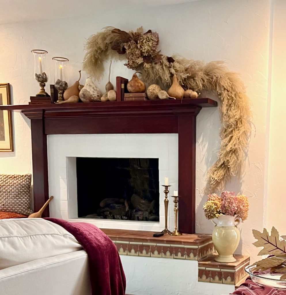 dramatic centerpiece of dried grasses, hydrangeas and magnolia leaves is hung on the wall above a fireplace