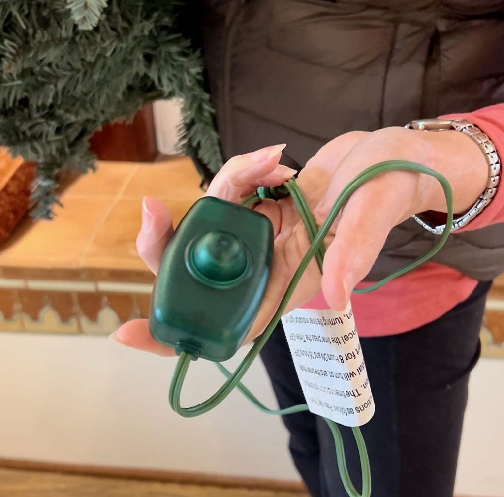 closeup of a woman's hand holding the foot activated power cord of a Christmas tree.