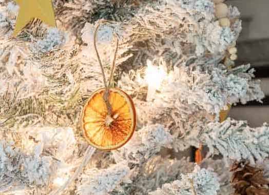 a dried orange slice is hung on a flocked Christmas tree with white lights all around
