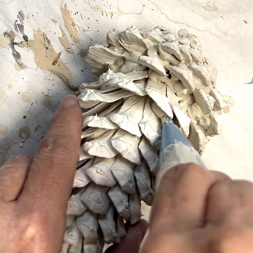 Woman is using a piping bag to apply joint compound in the crevices between pinecone scales