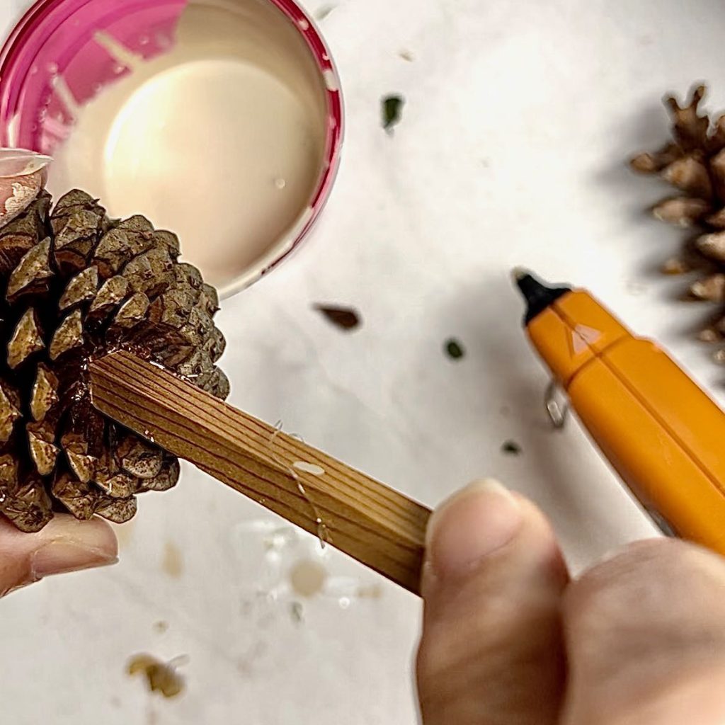 woman's hands attaching a wood stick to the base of a pinecone