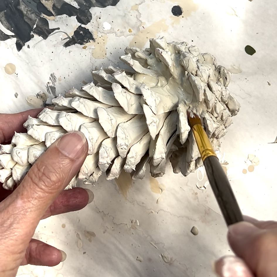 woman is using a paintbrush to smooth out the applied joint compound between the layers of pinecone scales