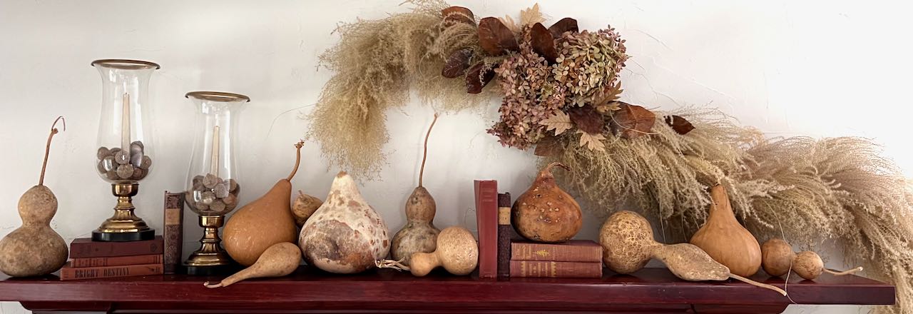 wide closeup of a wall-mounted dried arrangement hhanging above a mantel with gourds and vintage books