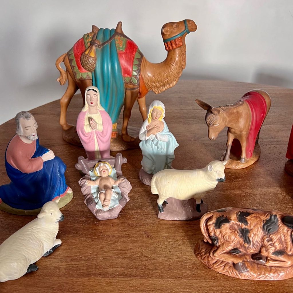 Mis-matched thrifted, bright colored nativity statues are lined up on a wood table
