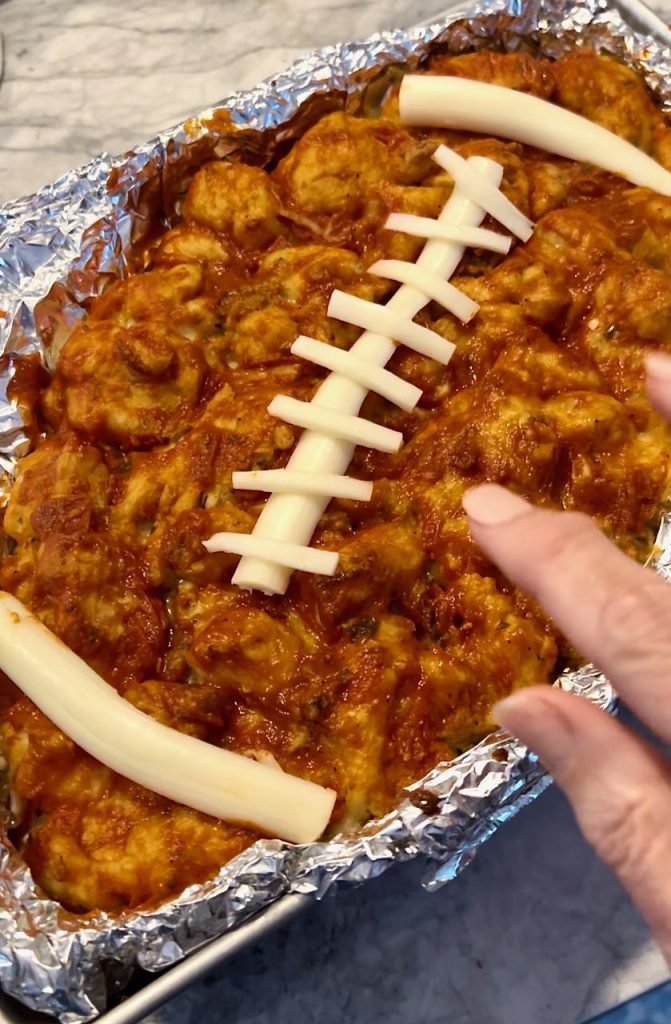 woman's fingers are arranging the lacing on the football shaped pizza