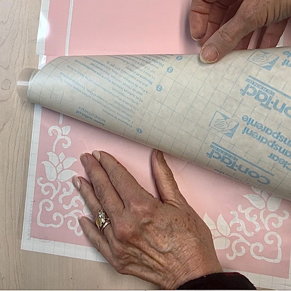 woman adding a clear contact paper to the weeded stencil to move it to the mat.