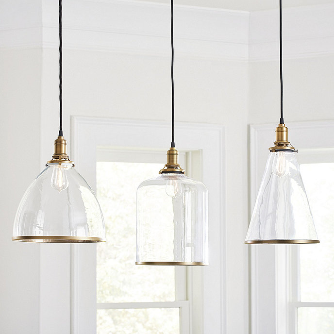 Three different clear glass globe pendant lights with gold metal rims around the bottom of the shades