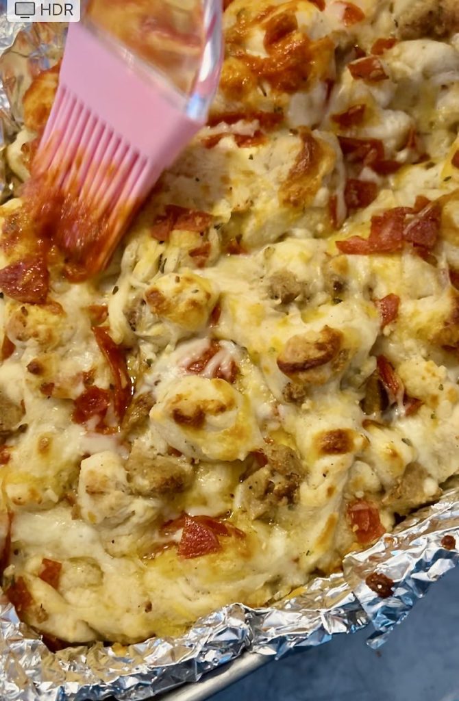 paartially cooked pull apart pizza is being basted with pizza sauce on top