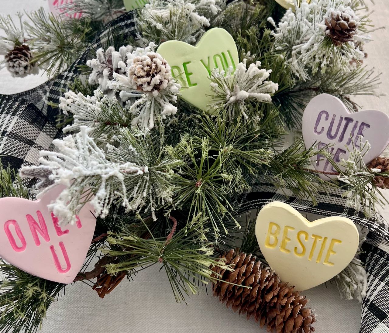 Closeup of large clay conversation hearts that say ONLY U, BESTIE, BE YOU and CUTIE PIE nestled in greenery of a centerpiece