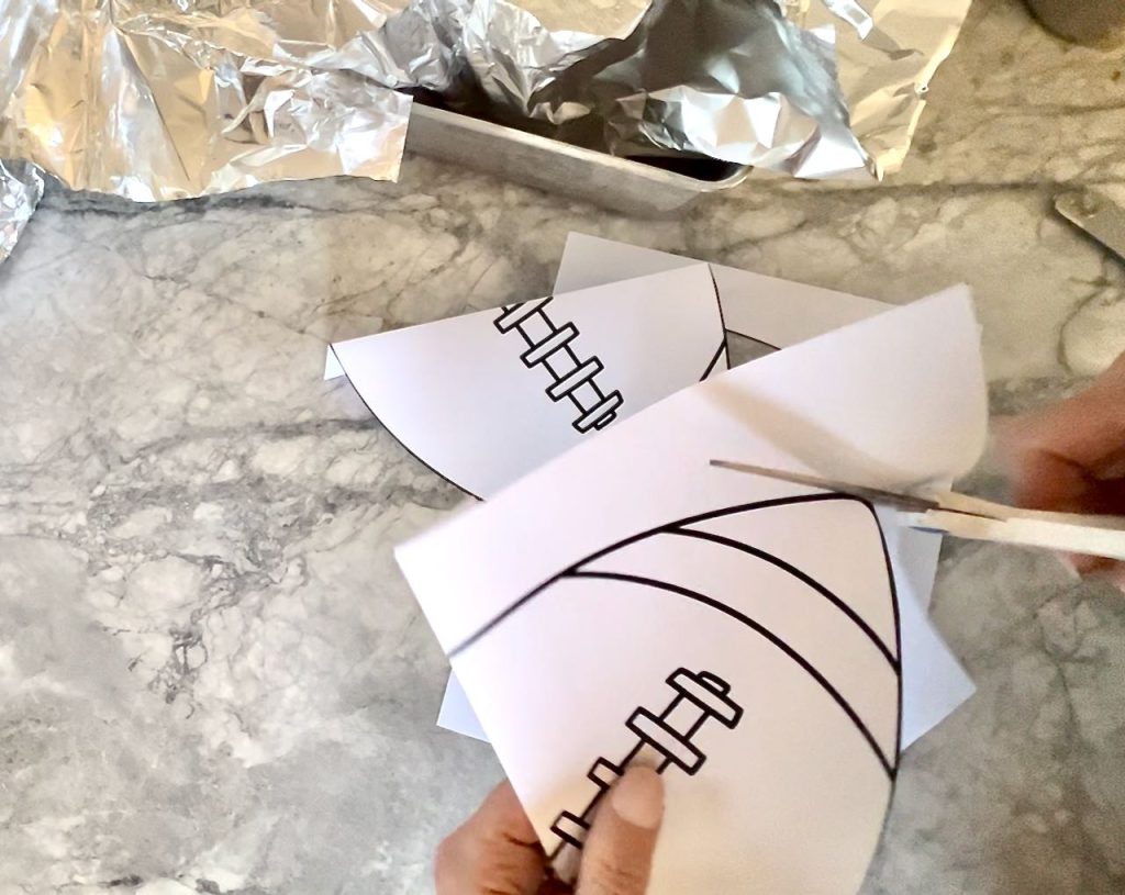 woman's hands cutting out the two ends of a football pattern on white paper