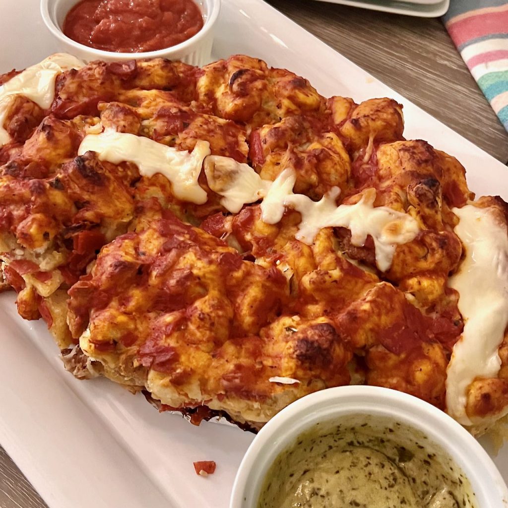 pull apart football shaped pizza is on a platter with bowls of pizza sauce and pesto aoli