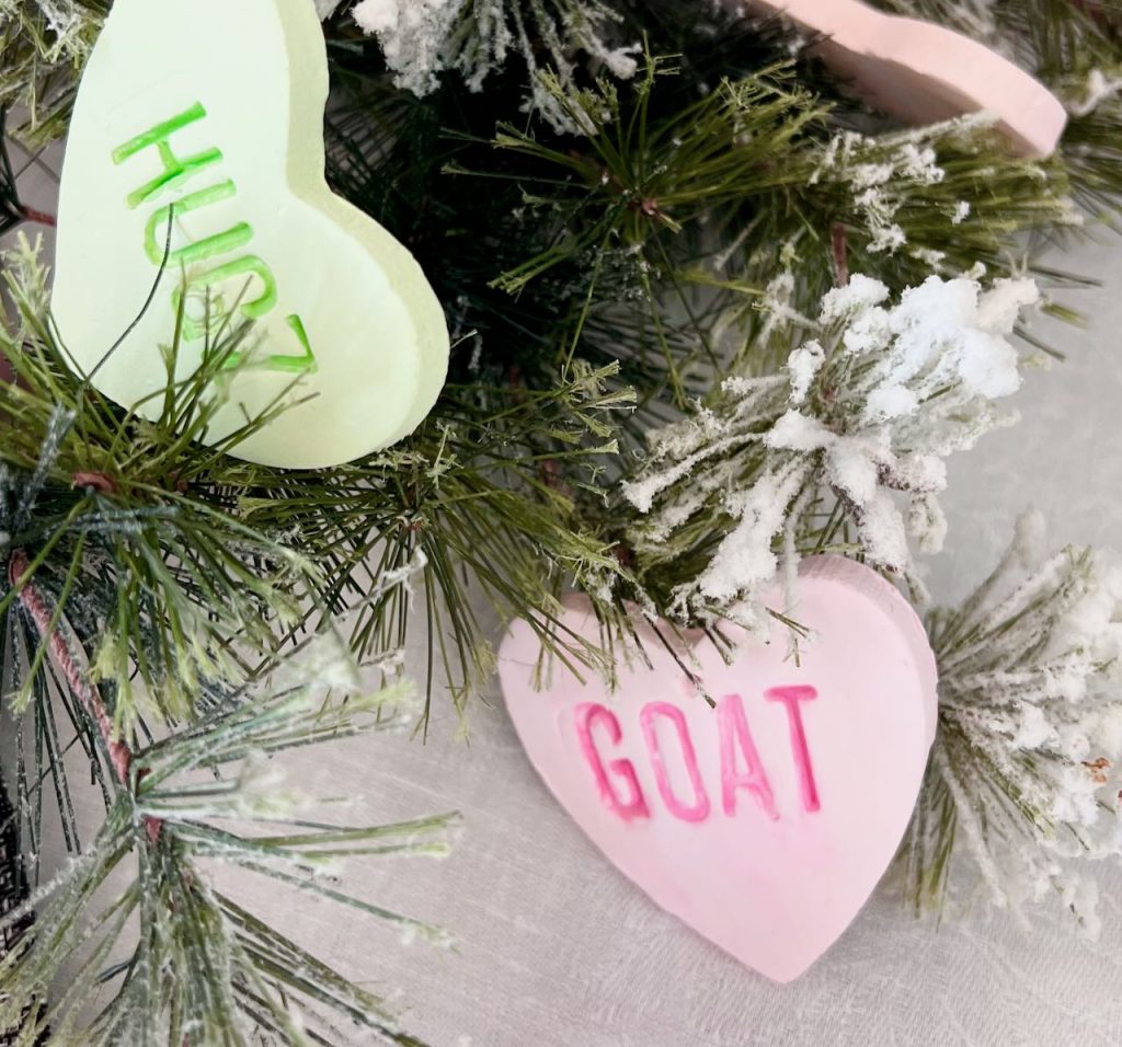 Closeup of large clay conversation hearts that say GOAT and HUGZ nestled in greenery of a centerpiece