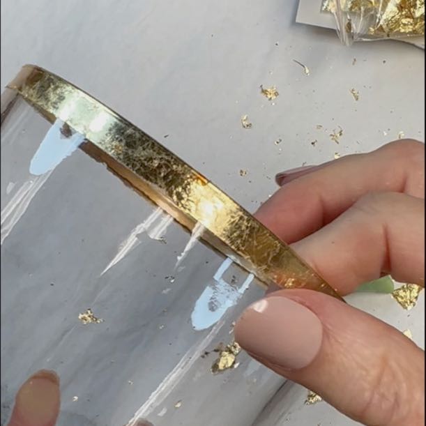 closeup of gold leaf flakes applied to the rim of a clear glass vase