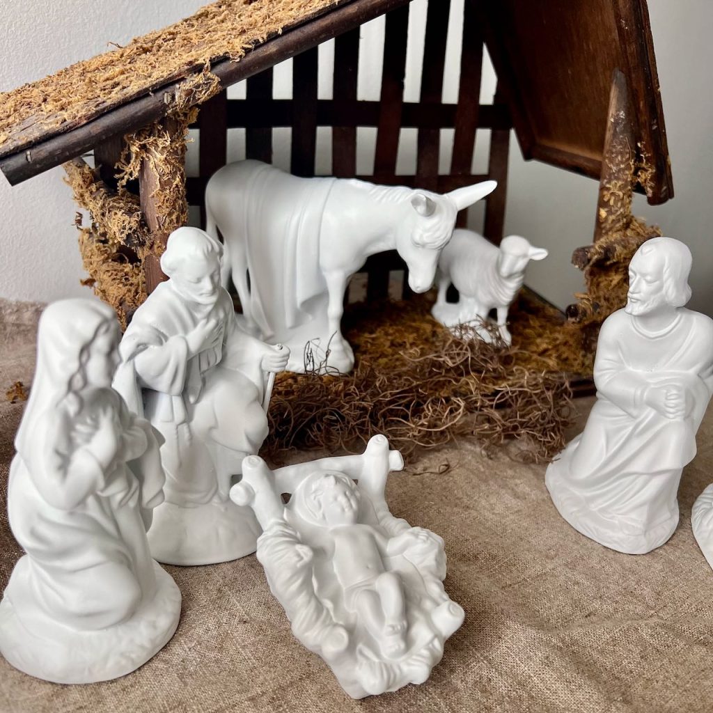 Old, mismatched nativity statues are now painted white in front of the manger