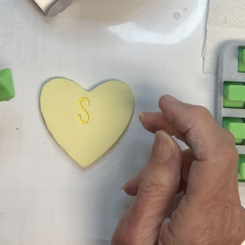 woman's fingers next to a clay heart with just an "S" stamped in the middle