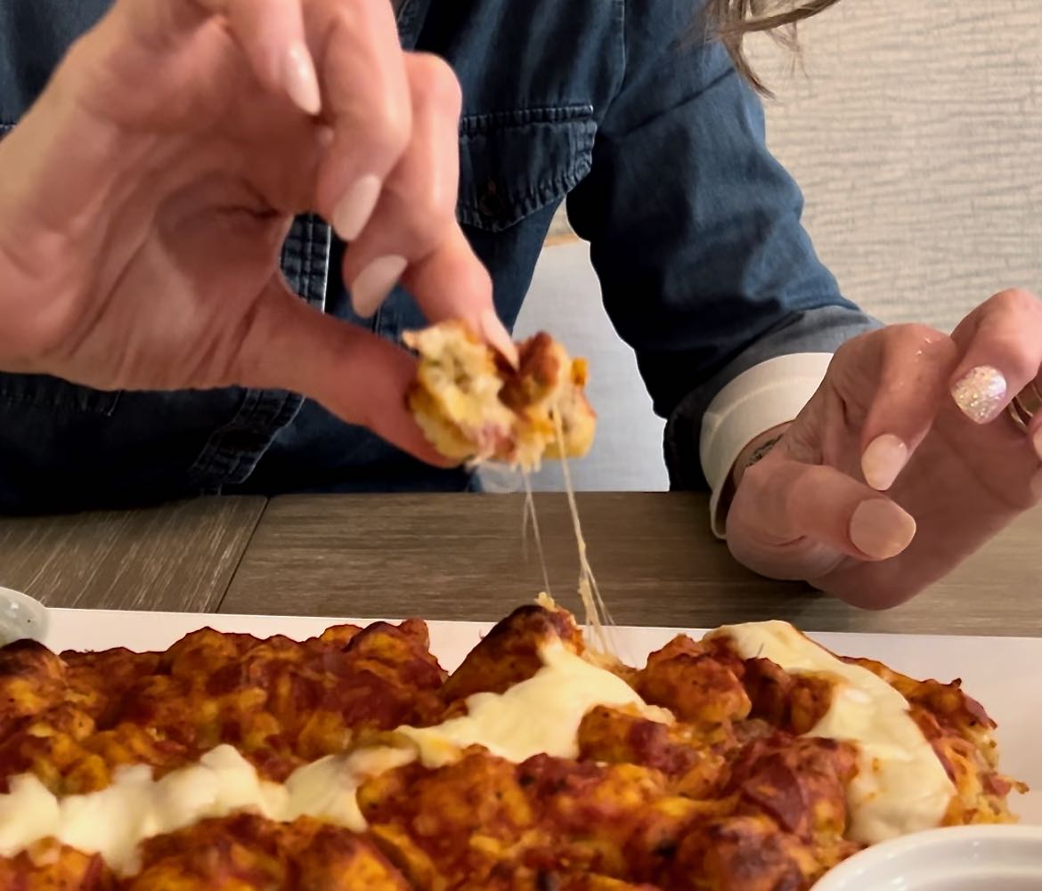 closeup of woman's hand pulling off a bite of pizza with the stringy gooey cheese pulliing with it