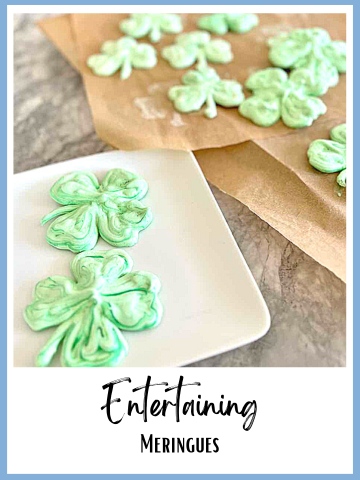Shamrock shaped meringue cookies on a plate and parchment covered baking sheet