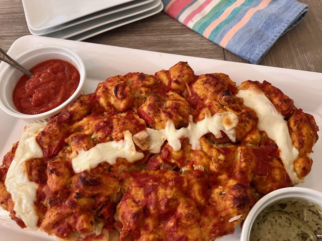 pull apart football shaped pizza is on a platter with bowls of pizza sauce and pesto dipping sauce